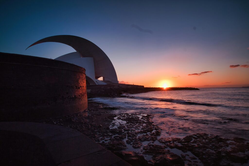Dramatic sunset illuminating Auditorio de Tenerife with ocean waves and twilight sky.