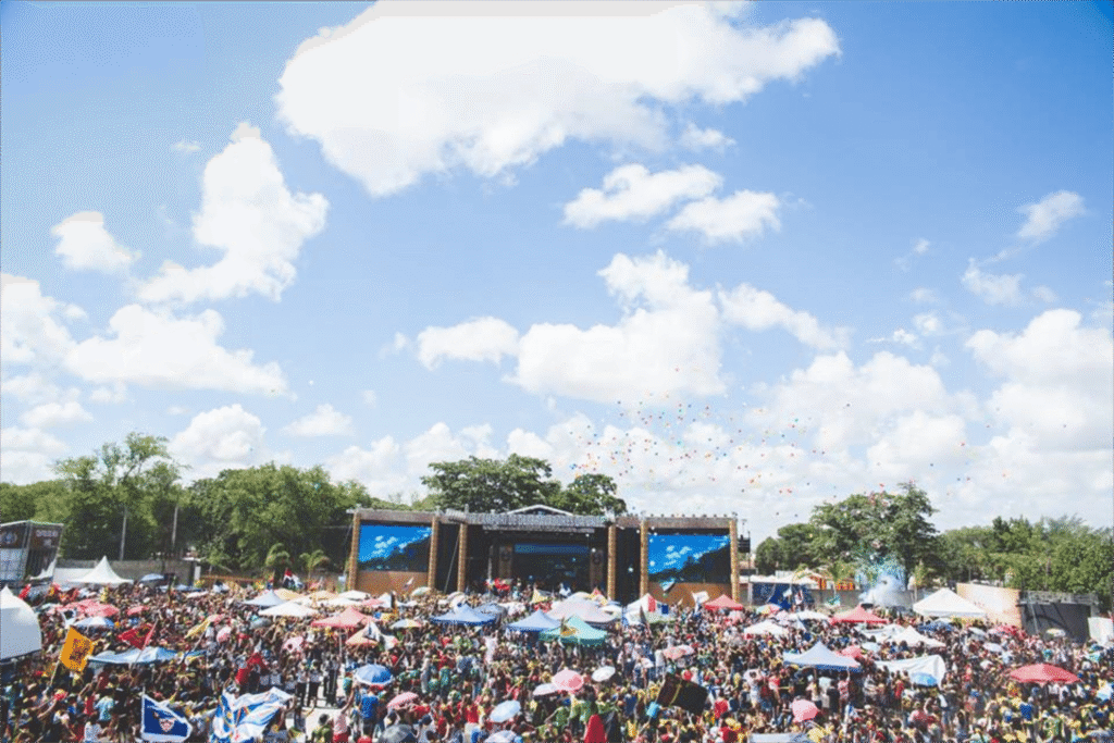Lively outdoor festival with large crowd, vibrant umbrellas, and a clear sky in Santos Reis, Brazil.